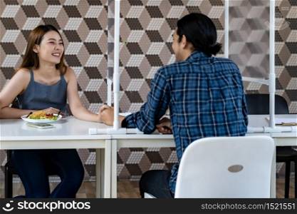 Asian young couple eating out together at new normal social distance restaurant with table shield partition reduce infection of coronavirus covid-19 pandemic. Restaurant new normal lifestyle.