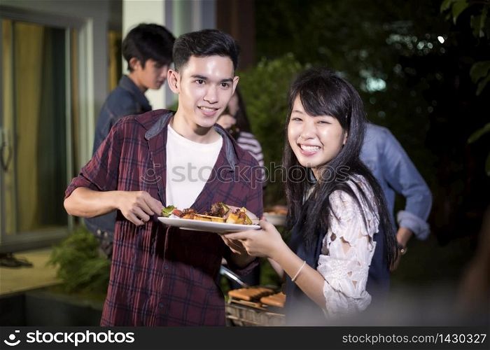 Asian young couple enjoying a romantic dinner and group of friends having outdoor garden barbecue laughing with alcoholic beer drinks on night