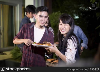 Asian young couple enjoying a romantic dinner and group of friends having outdoor garden barbecue laughing with alcoholic beer drinks on night