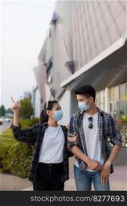 Asian Young Couple in protection mask standing outdoor of large building, They are discussion with happiness, New normal lifestyle amid coronavirus outbreak