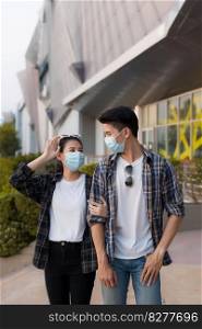 Asian Young Couple in protection mask standing outdoor of large building, They are discussion with happiness, New normal lifestyle amid coronavirus outbreak