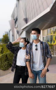 Asian Young Couple in protection mask standing outdoor of large building, They are discussion with happiness, New normal lifestyle amid coronavirus outbreak