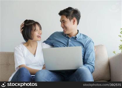 Asian young couple make fun of working on laptop. they sit on sofa in the contemporary living room.