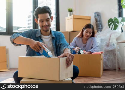 Asian young couple packing big cardboard box for moving in new home, Moving and House Hunting concept