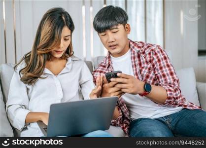 Asian Young couple sitting on sofa in living room at home use laptop computer and smartphone to working , talking and smile together with happiness, happy family concept