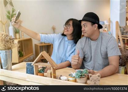 Asian Young Couple taking the selfie with happiness action in modern coffee shop or workplace or co-working space or modern office, lifestyle and leisure concept
