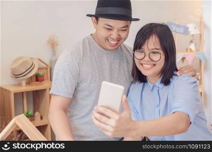Asian Young Couple taking the selfie with happiness action in modern coffee shop or workplace or co-working space or modern office, lifestyle and leisure concept