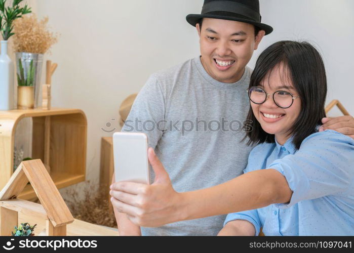 Asian Young Couple taking the selfie with happiness action in modern coffee shop or workplace or co-working space or modern office, lifestyle and leisure concept