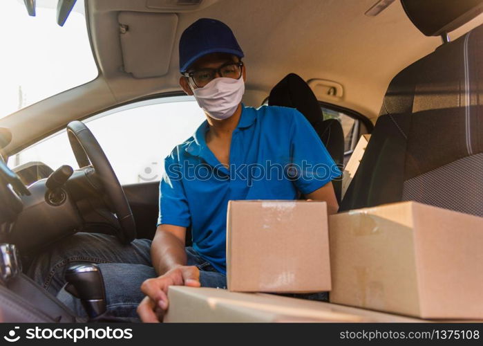 Asian Young delivery man courier online with boxes with uniform sitting in driving car he protective face mask, service customer on front house under curfew quarantine pandemic coronavirus COVID-19