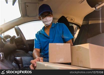 Asian Young delivery man courier online with boxes with uniform sitting in driving car he protective face mask, service customer on front house under curfew quarantine pandemic coronavirus COVID-19
