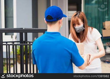 Asian young delivery man courier shopping online give package post box he protective face mask service woman customer receiving box at front home, under curfew quarantine pandemic coronavirus COVID-19