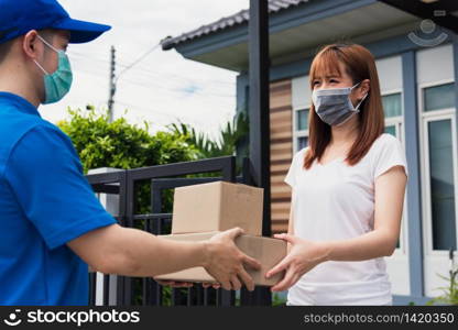 Asian young delivery man courier shopping online give package post box he protective face mask service woman customer receiving box at front home, under curfew quarantine pandemic coronavirus COVID-19