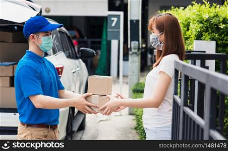 Asian young delivery man courier shopping online give package post box he protective face mask service woman customer receiving box at front home, under curfew quarantine pandemic coronavirus COVID-19
