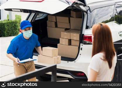 Asian young delivery man courier shopping online give parcel post box he protective face mask and service woman customer receiving boxed at front home door, under curfew pandemic coronavirus COVID-19