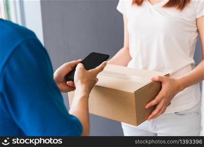 Asian young delivery man courier shopping online with package post box in uniform wearing protective face mask making service woman customer using hand finger signature on digital mobile phone at home