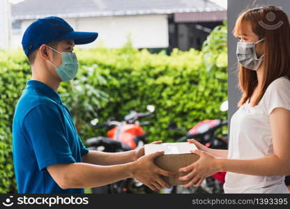 Asian young delivery man courier with package post box in uniform he protective face mask he making service woman customer receiving front house under curfew quarantine pandemic coronavirus COVID-19