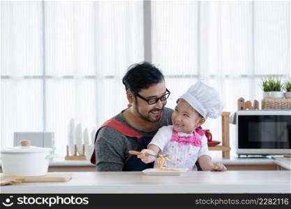Asian young father with beard and little cute mixed race daughter with apron and chef hat cooking and enjoy eating spaghetti together in kitchen at home. Family activity in special day concept