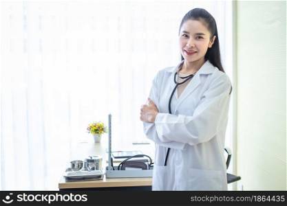 Asian young female doctor fold her arms with stethoscope with positive emotions in hospital background.