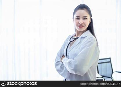 Asian young female doctor fold her arms with stethoscope with positive emotions in hospital background.
