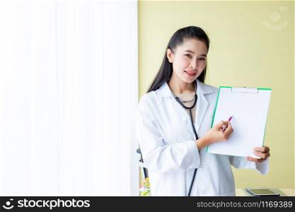 Asian young female doctor therapeutic advising with positive emotions hold empty clipboard and bed in hospital background,copy space