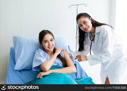 Asian young female doctor with syringe to the arm of Asian young female patient on Bed for better healing In the room hospital background.