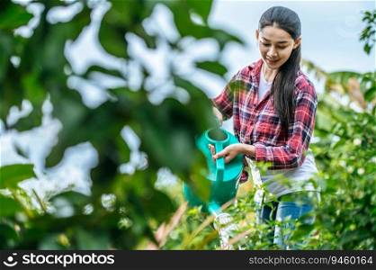Asian young female farmer watering plant in the green field. Modern technologies in agriculture management and agribusiness concept.