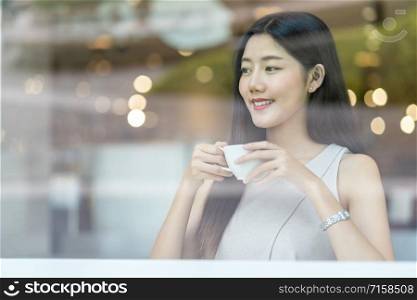 Asian young female holding a cup of coffee in modern coffee shop or coworking space beside window mirror,japanese,chinese,Korean lifestyle and daily life, entrepreneur concept
