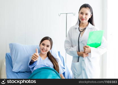 Asian young female patient on bed showing thumbs up with smiley face very good symptom to asian young female doctor in hospital background.