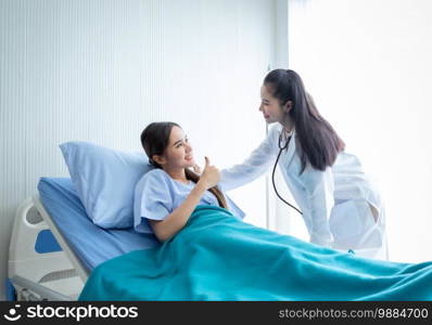 Asian young female patient on bed showing thumbs up with smiley face very good symptom to asian young female doctor in hospital background.