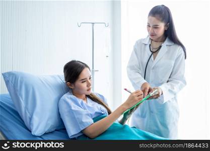 Asian young female patient Signature for consent form on bed to female doctor therapeutic advising with positive emotions in the room hospital background.