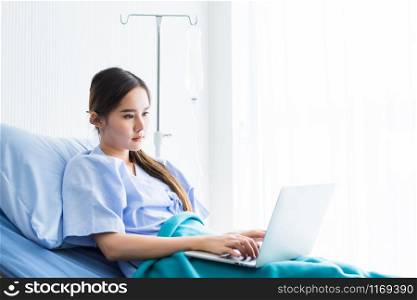 Asian young female patient smiley face working with laptop computer on bed in the room hospital background,concept of working business in a sick time