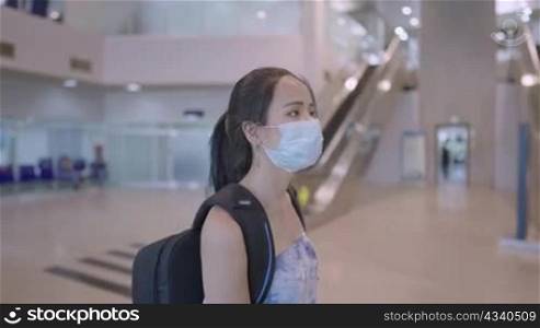 Asian Young female wear protective medical mask walking with backpack at airport terminal escalator area, risk of travel in public transportation, new normal pandemic outbreak, covid19 Corona virus