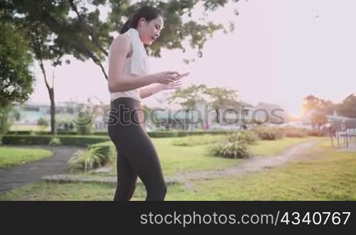 Asian young female wear sport clothing using smartphone while exercising at outdoor park, at sunset relax single woman lifestyle, wireless digital technology portable gadget mobile application user