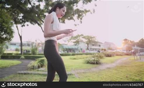 Asian young female wear sport clothing using smartphone while exercising at outdoor park, at sunset relax single woman lifestyle, wireless digital technology portable gadget mobile application user