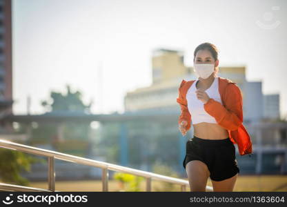 Asian Young fitness sport woman running and she wears a mask for protective Dust and pollution and protection flu virus, influenza, coronavirus on city