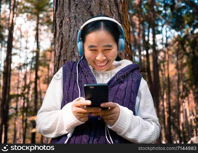 Asian young girl listening to music by headphone in the garden. Technology and relaxation concept.