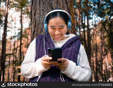 Asian young girl listening to music by headphone in the garden. Technology and relaxation concept.