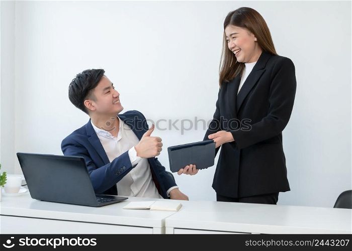 Asian young handsome businessman wear formal suit thumbs up for admire his colleagues for good ideas performance on tablet with smiling face. Happy business people in workplace where they was accepted