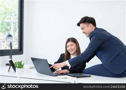 Asian young handsome businessman wear formal suit working with colleagues woman pointing on laptop with smiling face. Happy business people in workplace where they was accepted concept