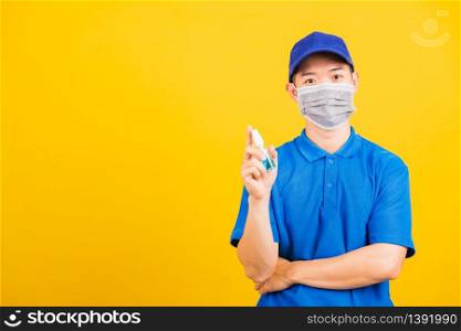 Asian young handsome delivery man wearing face mask protective germ virus and show alcohol sanitizing sprays on hand, studio shot isolated on yellow background, medical outbreak coronavirus COVID-19
