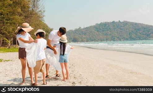 Asian young happy family activists collecting plastic waste on beach. Asia volunteers help to keep nature clean up and pick up garbage. Concept about environmental conservation pollution problems.