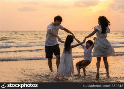 Asian young happy family enjoy vacation on beach in the evening. Dad, mom and kid relax playing together near sea when silhouette sunset. Lifestyle travel holiday vacation summer concept.