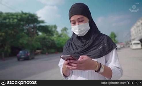 Asian young Islam Hijab woman wear protective medical mask. woman using mobile phone while walking on the street side, car passing on background network connection, COVID-19 pandemic new normal