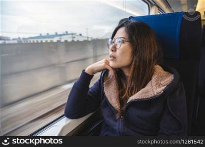 Asian Young lady passenger Sitting in a depressed mood beside the window inside Train which travel between town when travel alone for escape the chaos, traveller and depress concept