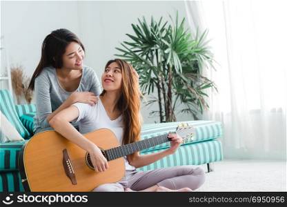 Asian young lesbian couple playing guitar for her lover with love moment in the bedroom surrounded with warm sunlight. LGBT couple have a love moment together ion the bed. LGBT love moment concept.