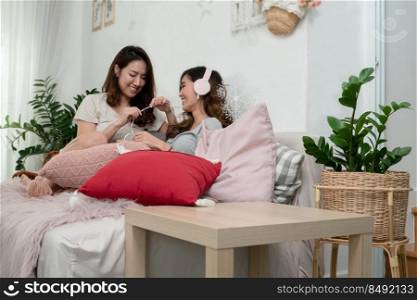 Asian young LGBT women couple with headphones enjoy listening music. Lovely girls smiling relaxing and sitting on sofa together in living room at home. LGBT relationship lifestyle concept