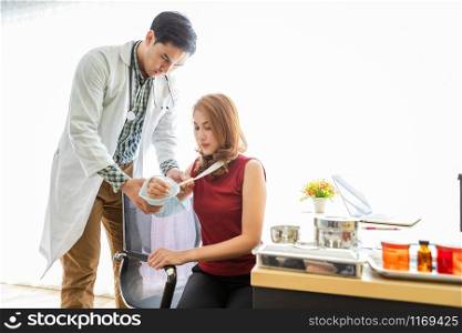 Asian Young man doctor of checking splint the arm of female patient hand due to with her arm broken for better healing sit in a wheelchair In the room hospital background.