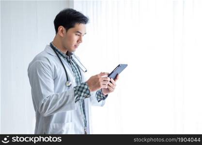 Asian Young man doctor therapeutic advising with positive emotions holding up and showing digital tablet in hospital background,copy space