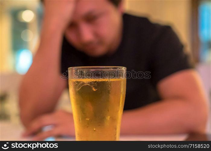 Asian young man in lonely and depressed action and holding head in hands and see glass of beer in pub and restaurant with low light place, depression and drinking concept