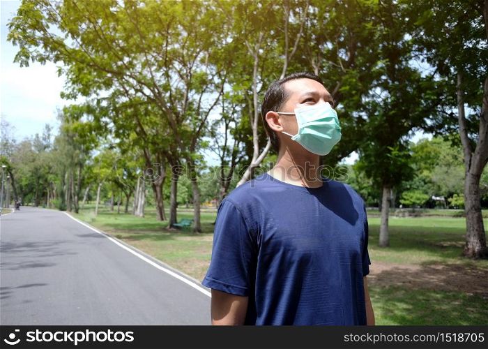 Asian young man in sportwear and wearing mask protection for covid-19 virus and exercise for running and jogging in the garden. Social distancing and new normal life Concept